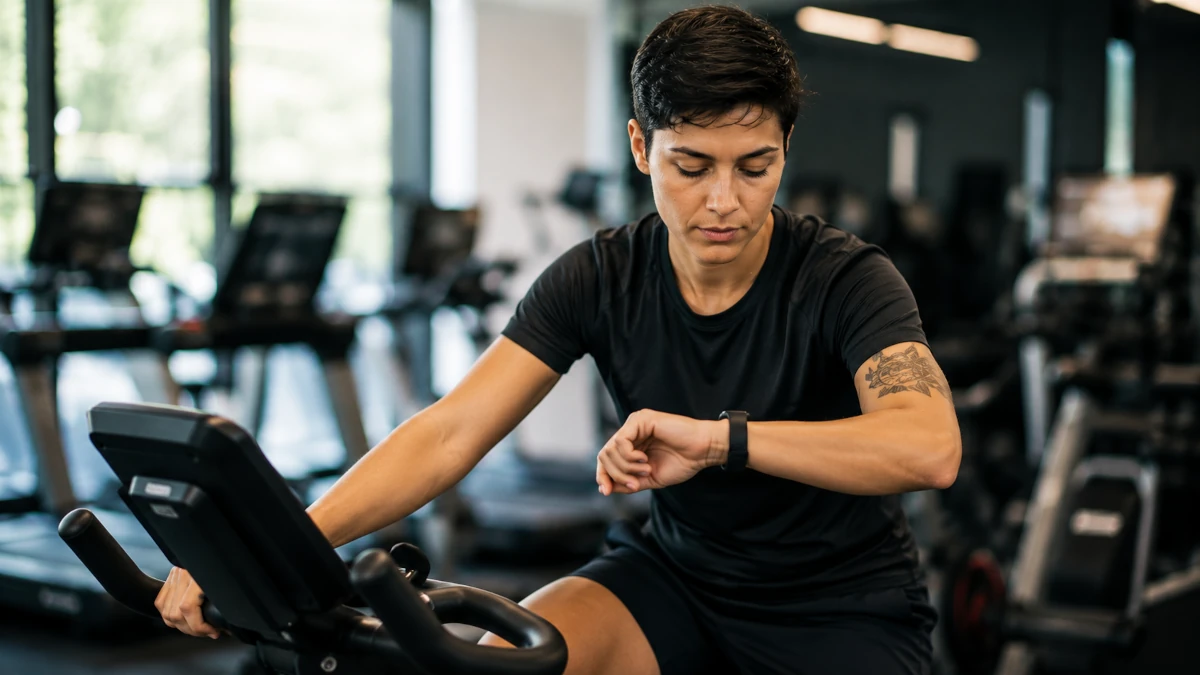 Person on a stationary bike at a gym glancing at their wrist tracker, checking heart rate during a workout
